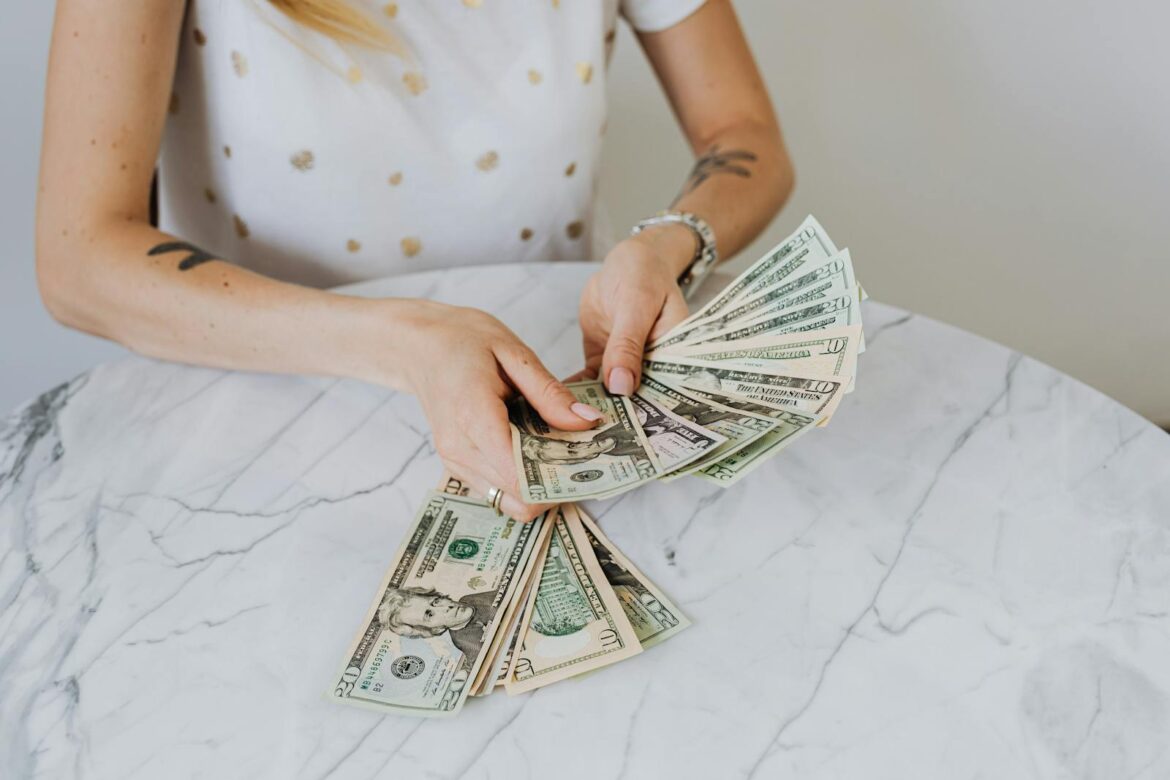 Close-up of a person counting US dollar bills on a luxurious marble table, symbolizing wealth and finance.