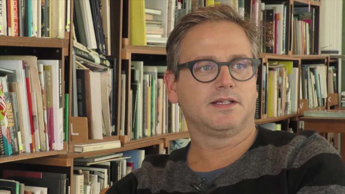 Guus Meeuwis tijdens een interview voor een boekenkast